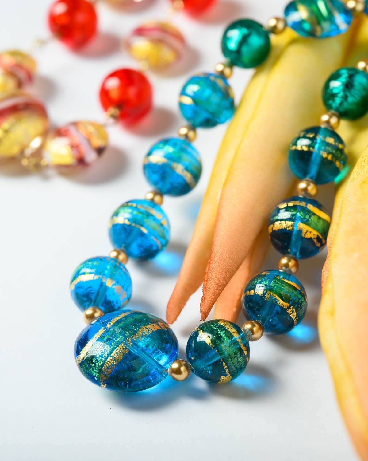 Close-up of a Murano necklace with vibrant blue beads featuring gold accents, displayed on a decorative surface